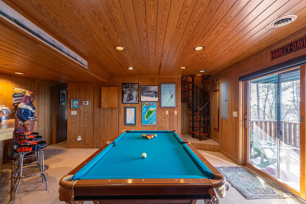A game room featuring a pool table, spiral staircase, wood paneling, and framed art. The casual setting invites playful interaction, with the spiral staircase serving as a notable architectural feature. The scene exudes a sense of fun and informal socializing, ideal for both adults and kids.