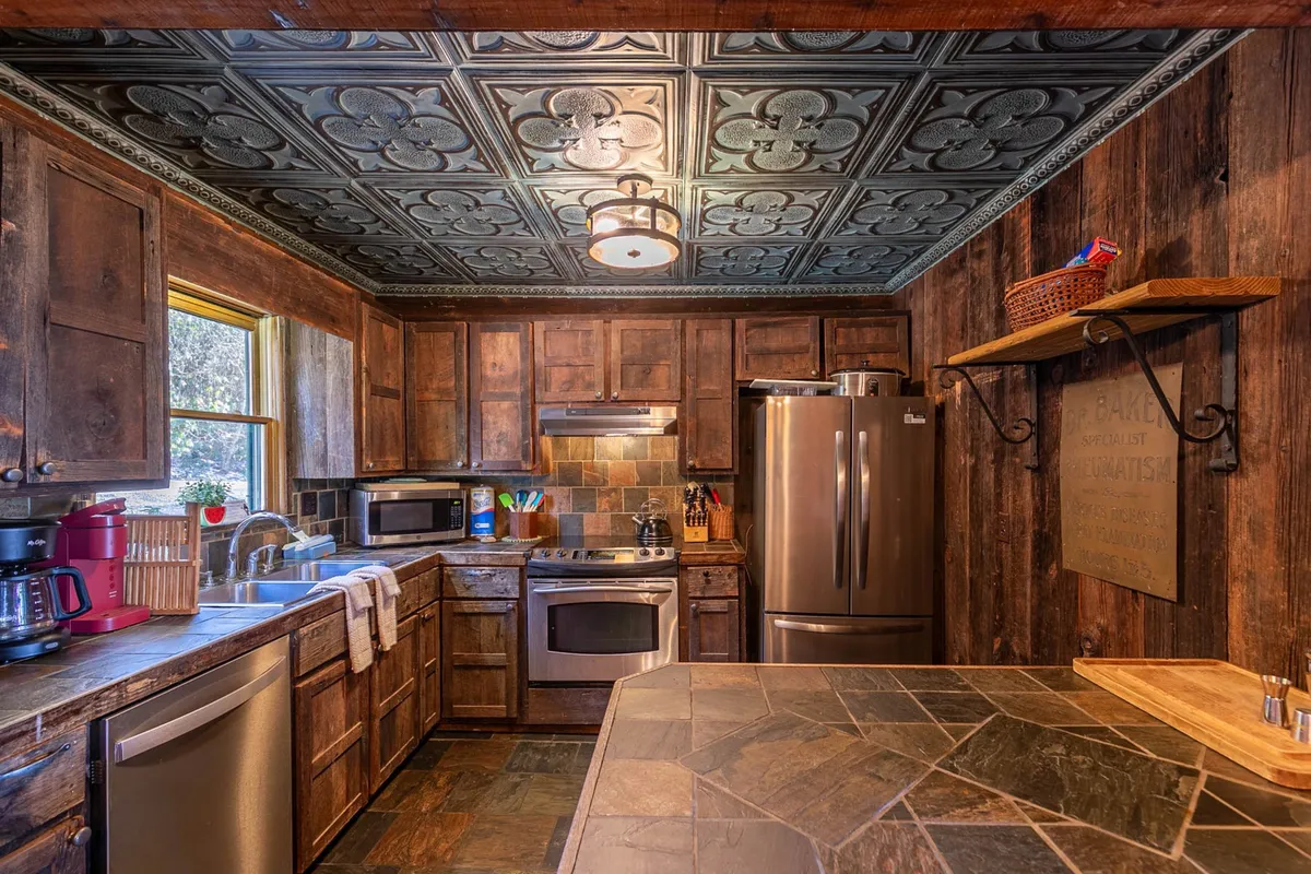 A view of the kitchen with wooden cabinetry, stainless steel appliances, a decorative ceiling, and stone countertops. The space feels warm and rustic, suggesting a place where family meals are prepared together and memories are made.