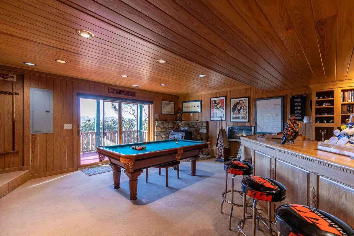 A spacious and bright entertainment area featuring a pool table, sleek bar area, and large windows that let in natural light. The space is arranged for both play and conversation, with plenty of room for guests to mingle or relax between games.