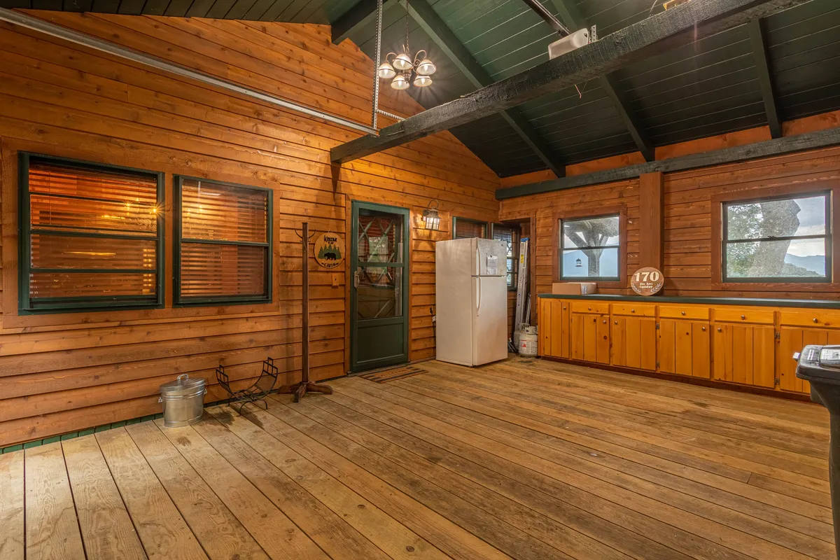 The image shows an inviting kitchen and living area with large windows and wooden walls, allowing natural light to pour in. The kitchen area opens up to the outside, hinting at easy access to the surroundings and shared moments after outdoor explorations.