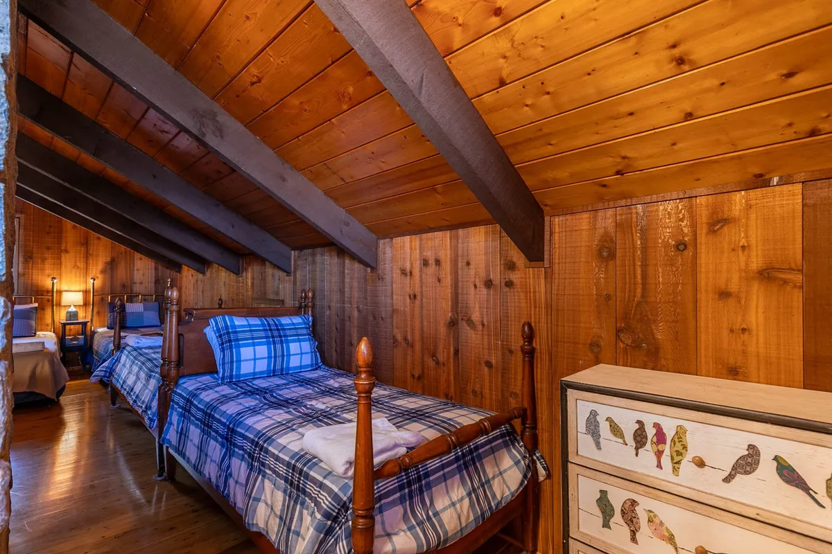 A charming loft area with exposed wooden beams, two twin beds with cozy bedding, and a colorful dresser. The playful setup and open feel create a perfect space for children or flexible sleeping arrangements for adults.