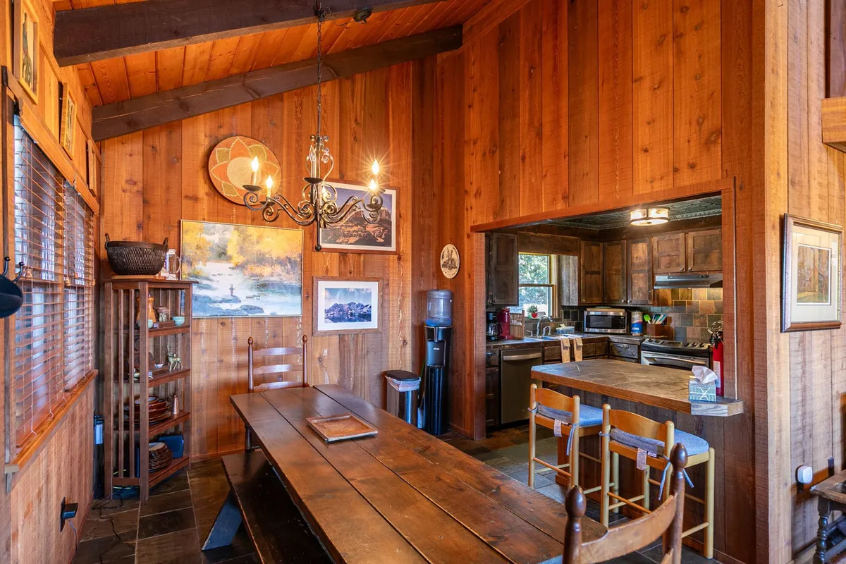 A long wooden dining table set beneath a distinctive chandelier, accented by exposed wooden beams and tasteful art on the walls. The scene exudes warmth and is set for an intimate, communal meal.