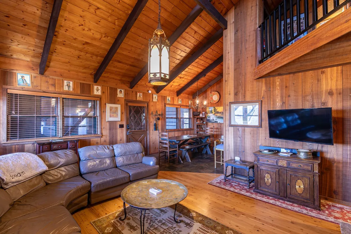 A warm and welcoming interior scene features a spacious living area with a leather sofa, coffee table, and wooden beams. There is plenty of room for people and pets to relax together, suggesting comfort and togetherness.